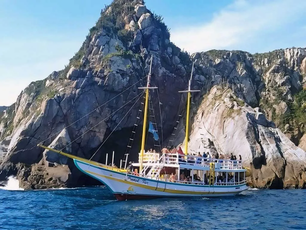 Passeio de barco em Arraial do Cabo, explorando a Ilha do Farol. Turistas desfrutam do mar azul e do cenário paradisíaco.