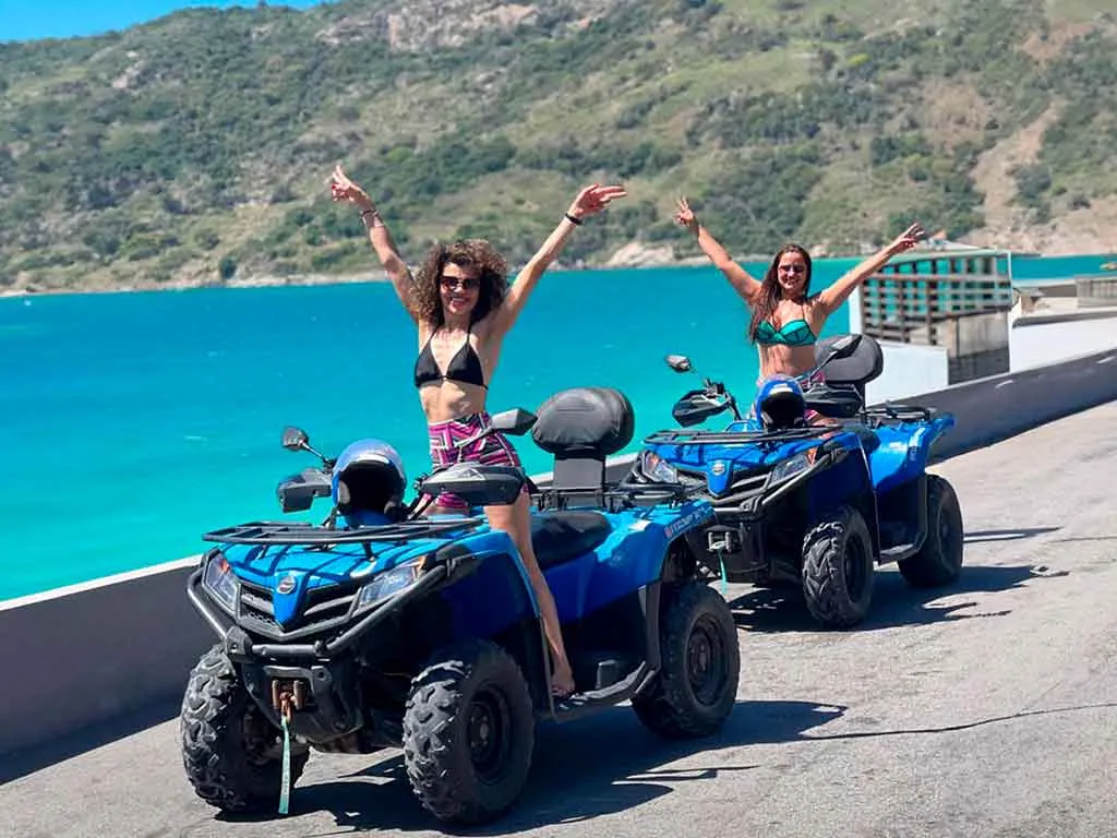 Turistas fazendo trilha em Quadriciclos em Arraial do Cabo, com montanhas e vista para o mar ao fundo.